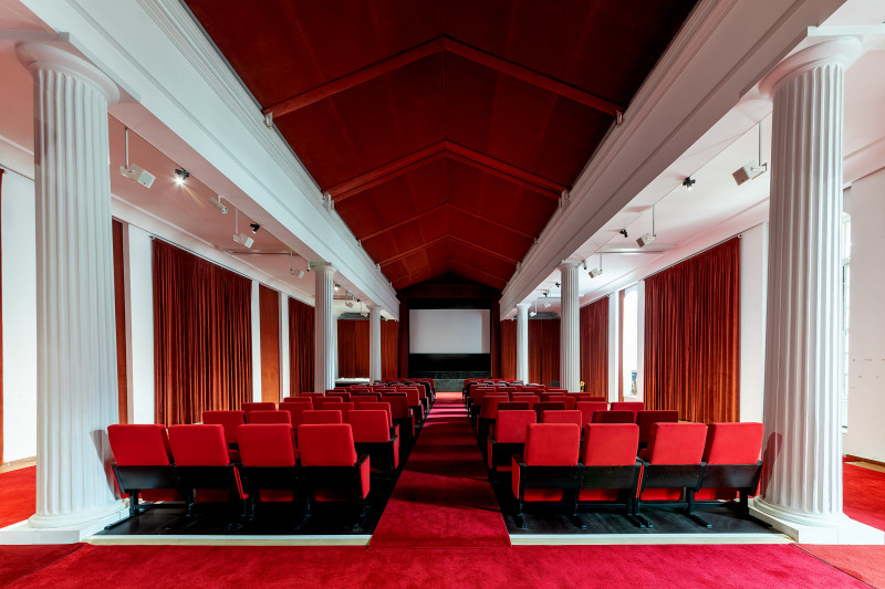 Na pierwszym planie czerwone fotele sali kinowej, w  oddali ekran 